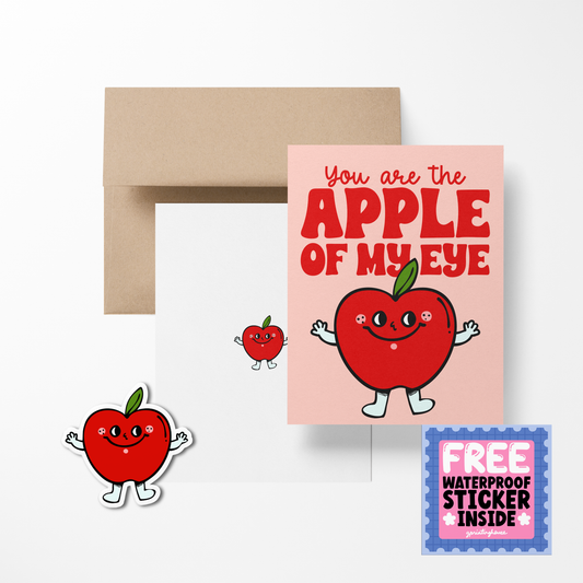 A greeting card with a illustration of a red apple with facial features and arms, accompanied by the phrase 'You are the APPLE of my EYE'. There is also a brown envelope and a free waterproof vinyl sticker included.