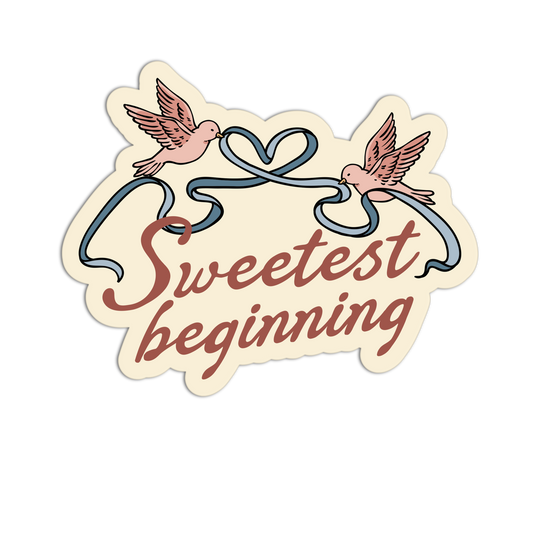 A die-cut sticker with the phrase 'Sweetest beginning' in cursive script, featuring two pink doves holding a blue ribbon that forms a heart at the top, on a cream background with a thin black outer border.