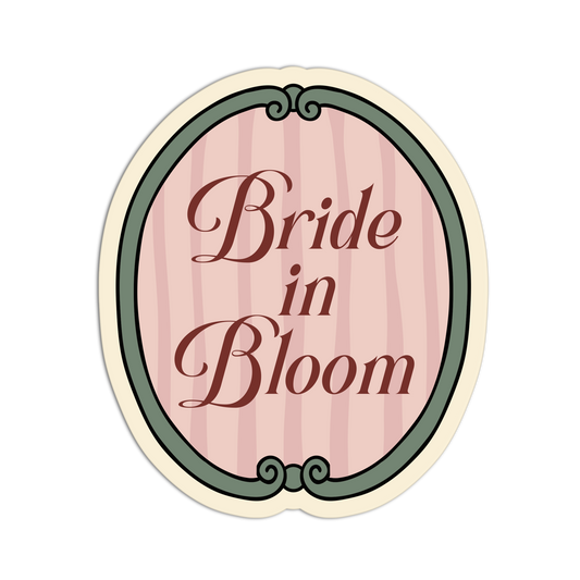 An oval-shaped decorative sticker or label with the words 'Bride in Bloom' in dark brown script over a pale pink vertically striped background, framed by a muted green border and cream outer edge on a white background.