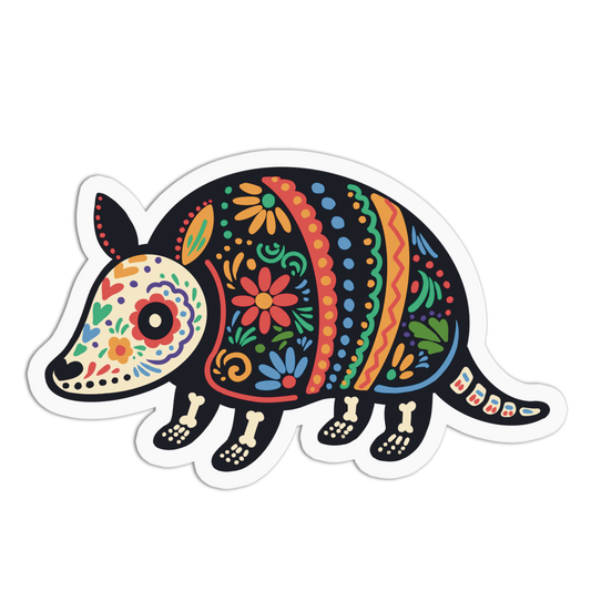 A die-cut vinyl sticker of an armadillo decorated with colorful Mexican Day of the Dead (Dia de los Muertos) patterns, shown on a solid white background.
